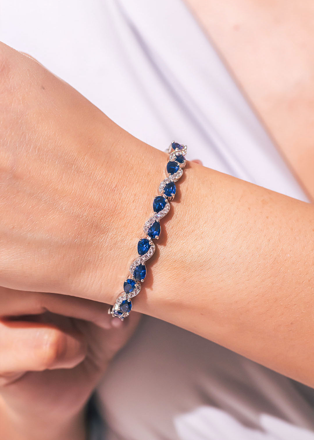 Deep blue pear-cut tennis bracelet with S-shaped pavé links, close-up worn on model's wrist – Duavaa